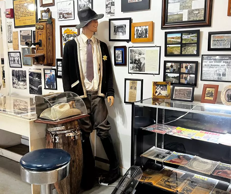 Museum exhibit at the Bonnie and Clyde Ambush Museum featuring a lawman mannequin, vintage photos, artifacts, and memorabilia on display.