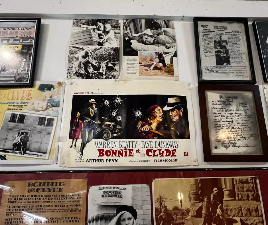 Wall display inside the Bonnie and Clyde Ambush Museum featuring vintage movie posters, crime scene photos, newspaper clippings, and memorabilia about the infamous outlaw couple.