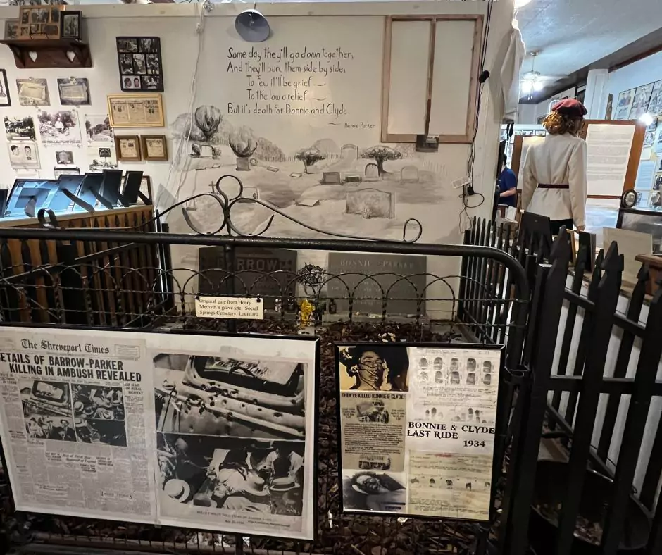 Bonnie and Clyde museum display with historic newspapers, photos, and a replica of their gravestone inside a fenced exhibit.