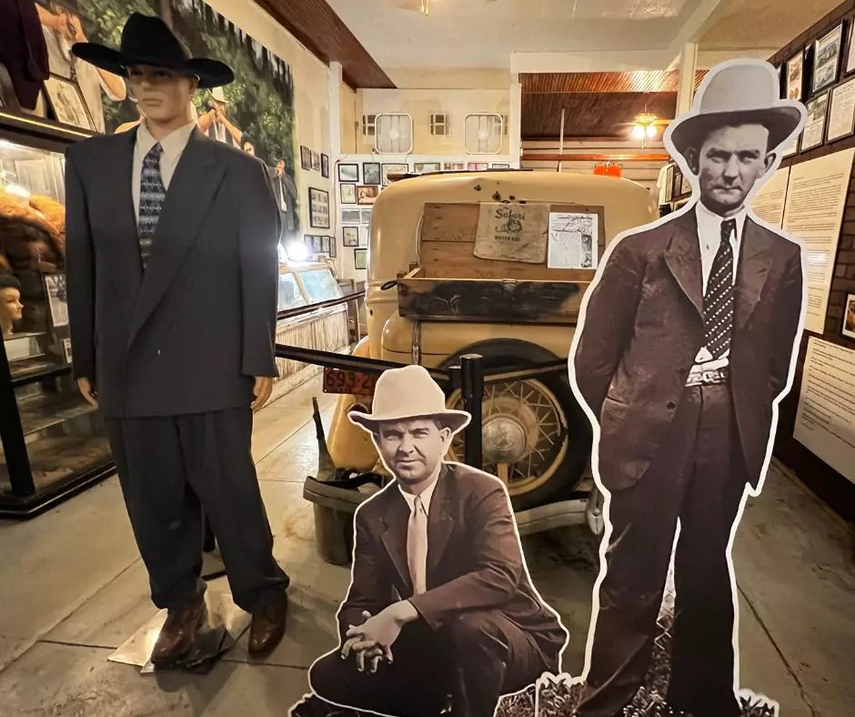 Mannequin and cardboard cutouts of lawmen displayed inside the Bonnie and Clyde museum with vintage car in the background.