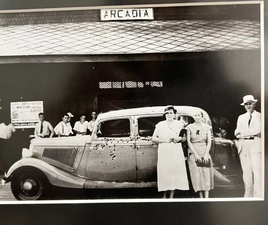 Archival black-and-white photograph showing bystanders gathered around Bonnie and Clyde’s bullet-riddled car in Arcadia.