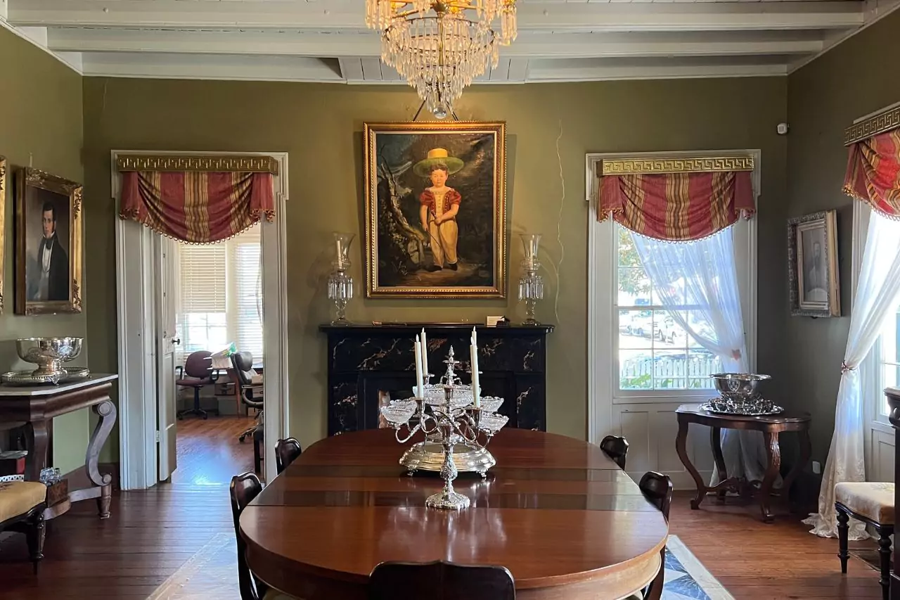 Elegant Dining Room at Lafayette Museum Historic dining room at Lafayette Museum with polished wood table, silver candelabra centerpiece, crystal chandelier, and 19th-century paintings including a portrait of a child in straw hat above a black marble fireplace.
