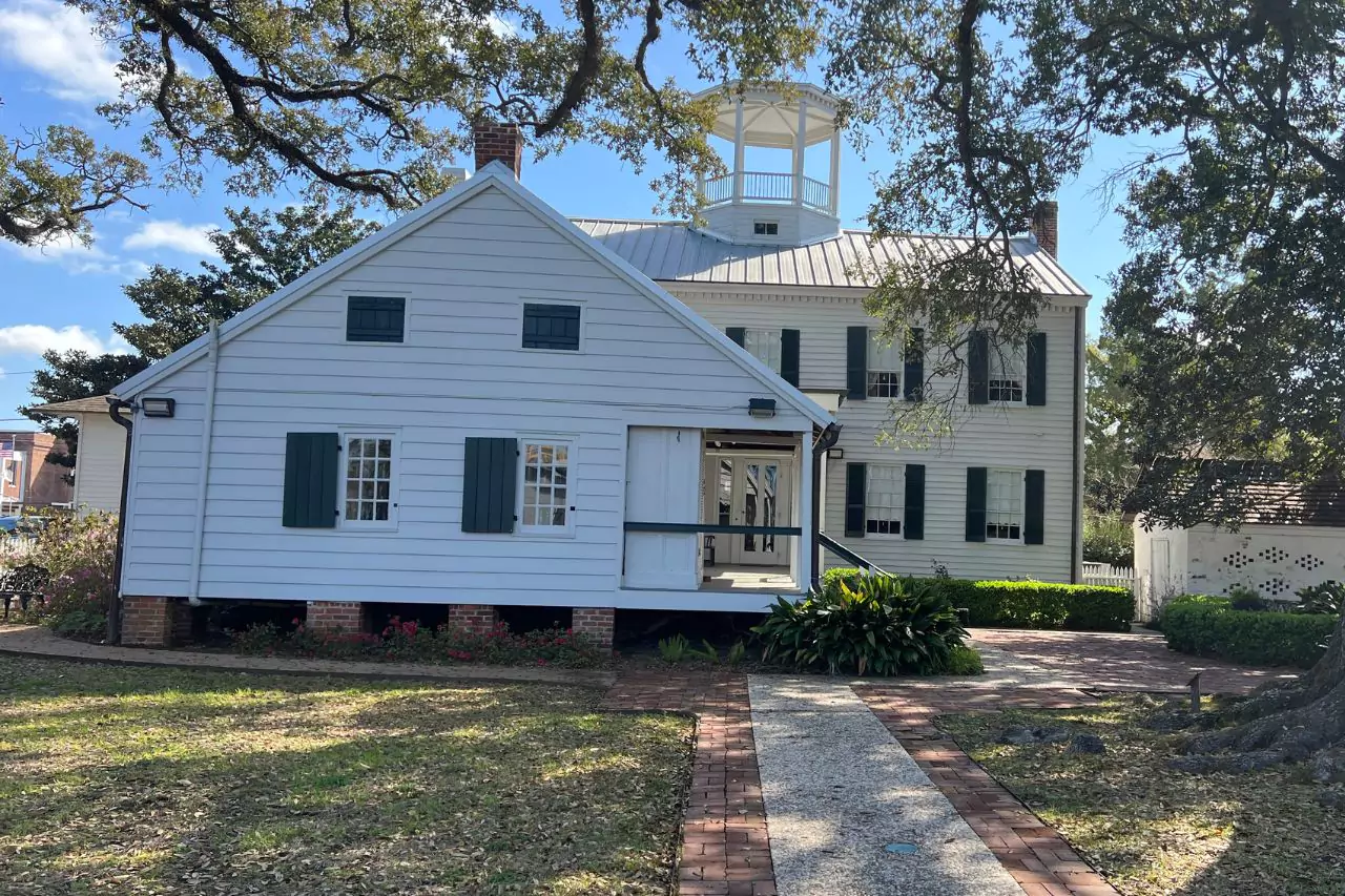 Rear View of Lafayette Museum Buildings White wooden outbuilding and main structure of Lafayette Museum with cupola, green shutters, and brick pathways surrounded by oak trees and manicured gardens.