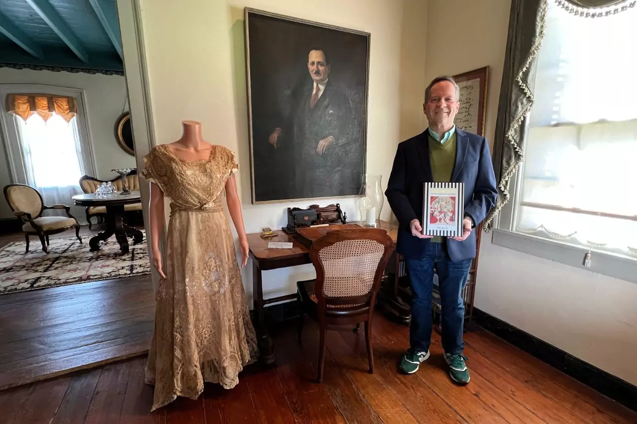 Exhibit Room with Historical Fashion and Portrait Lafayette Museum interior with a gold vintage gown on mannequin, man holding framed artwork, historic portrait of a suited man, and antique desk with typewriter.