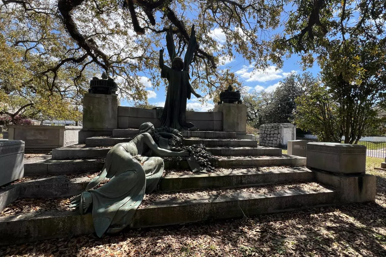 Grave Monument with Bronze Sculptures in Cemetery Dramatic bronze cemetery monument at Lafayette Museum with angelic and mourning female sculptures atop stone steps, shaded by sprawling oak trees and surrounded by tombs.