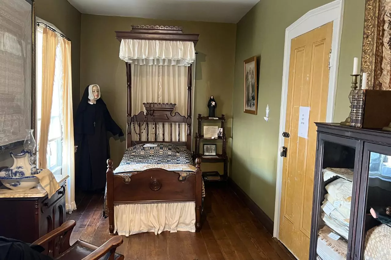Canopy Bed and Nun Mannequin in Historic Bedroom Period bedroom at Lafayette Museum featuring ornate wooden canopy bed, nun mannequin, vintage quilt, washstand, and religious-themed decor.