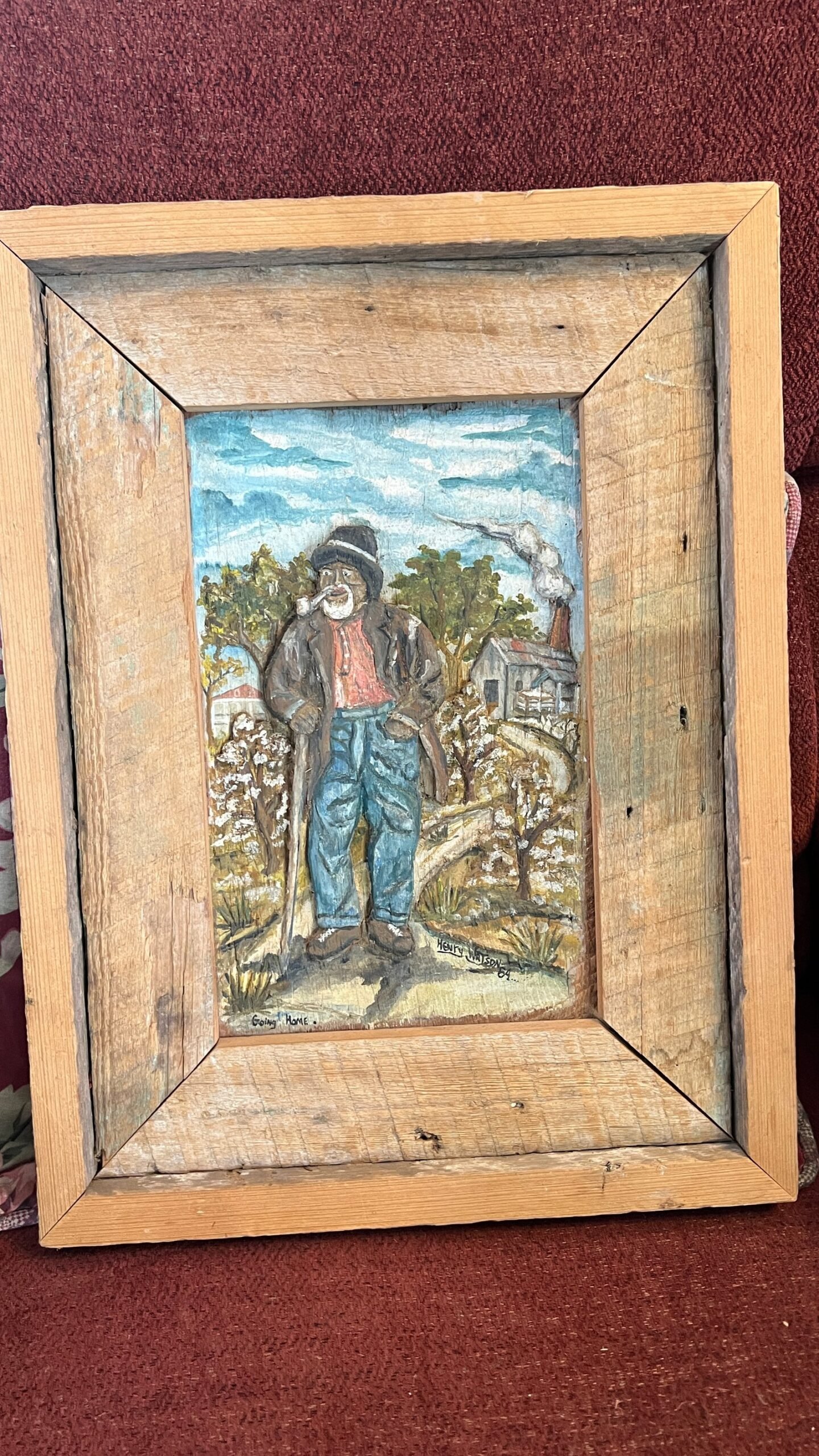 "Going Home" by Henry Watson, framed carving of a man standing in a cotton field with homes and smokestacks in the distance, created on reclaimed wood.