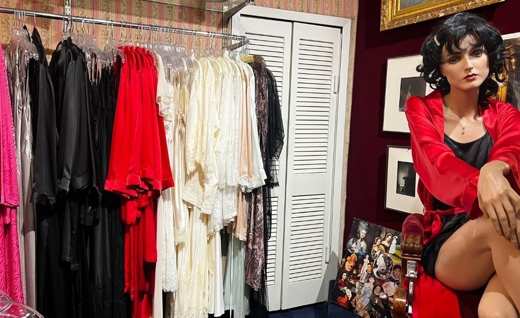 Clothing racks with elegant black, white, and red garments, beside a mannequin styled in vintage attire and framed photos on the wall.