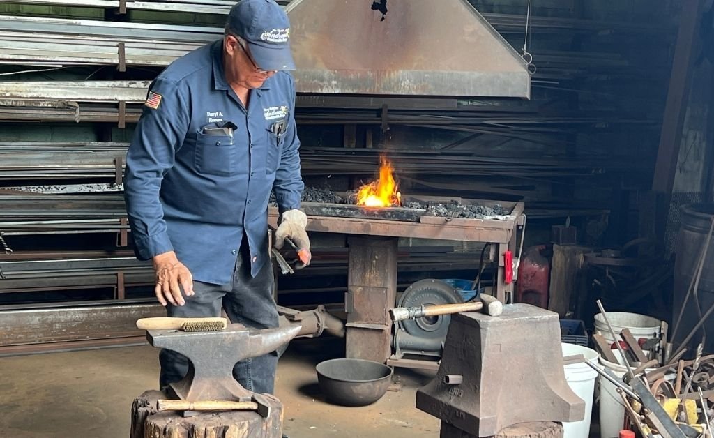 Master blacksmith Darryl Reeves working at the anvil in his 7th Ward forge, with fire burning in the background as he shapes iron by hand.