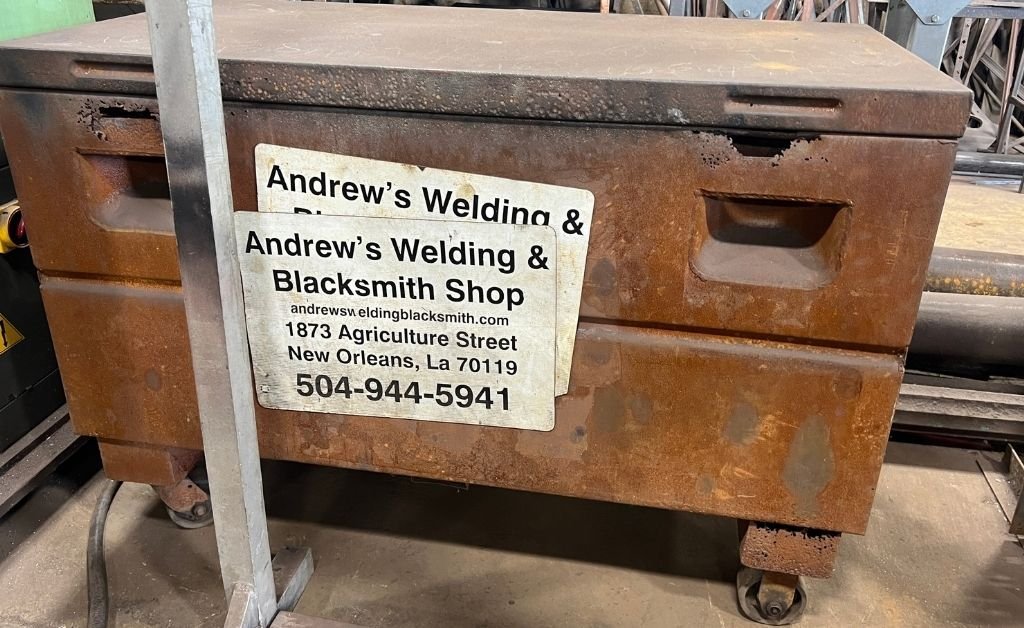 A rusted metal storage box inside Andrew’s Welding & Blacksmith Shop with a sign displaying the shop’s name, address, and phone number in New Orleans.