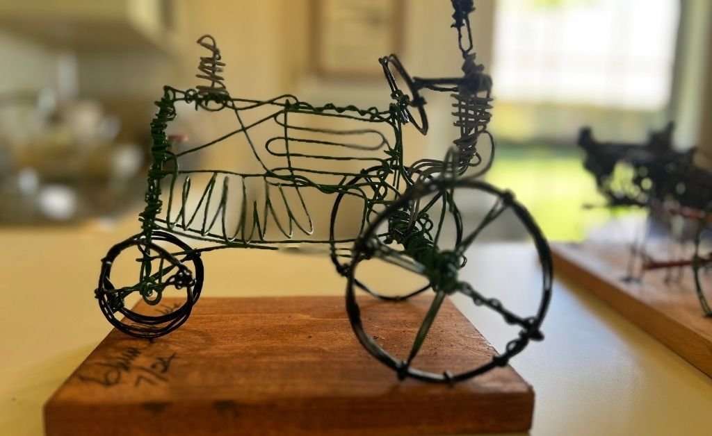 Close-up of a handcrafted wire toy tractor mounted on a wooden base, part of Elvin Shields’ folk art collection inspired by childhood experiences.