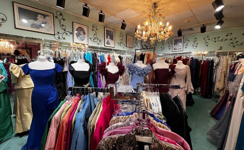 A chandelier-lit room inside Yvonne LaFleur’s boutique showcasing racks of colorful gowns and elegant mannequins, surrounded by framed portraits and ornate décor.