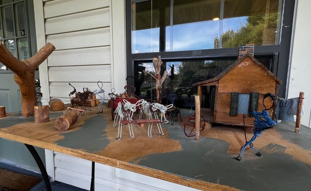 Miniature wire and wood diorama by Elvin Shields, depicting plantation life with handmade figures, oxen, wagons, and a cabin, displayed on a porch shelf.