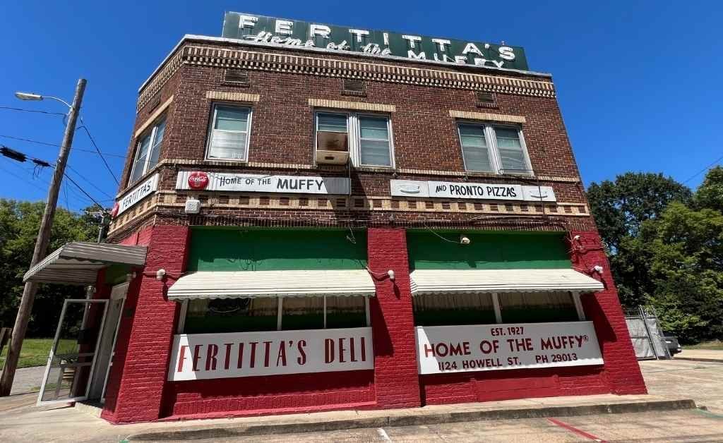 Exterior view of Fertitta's Deli in Shreveport, a two-story red brick building with green awnings and signs reading Home of the Muffy and Pronto Pizzas.