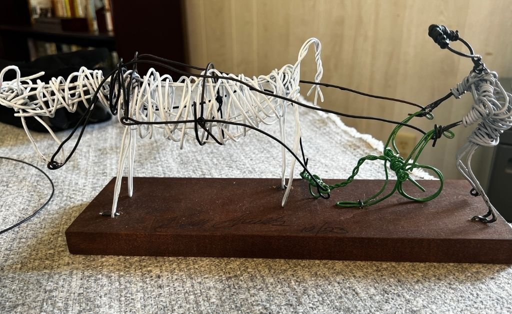 Wire sculpture by Elvin Shields showing a man pulling a plow with two mules.