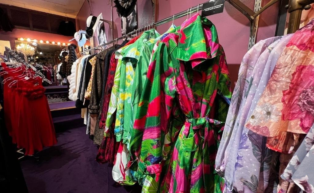 Racks of vibrant gowns in bold patterns and colors displayed inside Yvonne LaFleur’s New Orleans boutique, alongside hats and vintage décor that reflect the shop’s signature elegance.