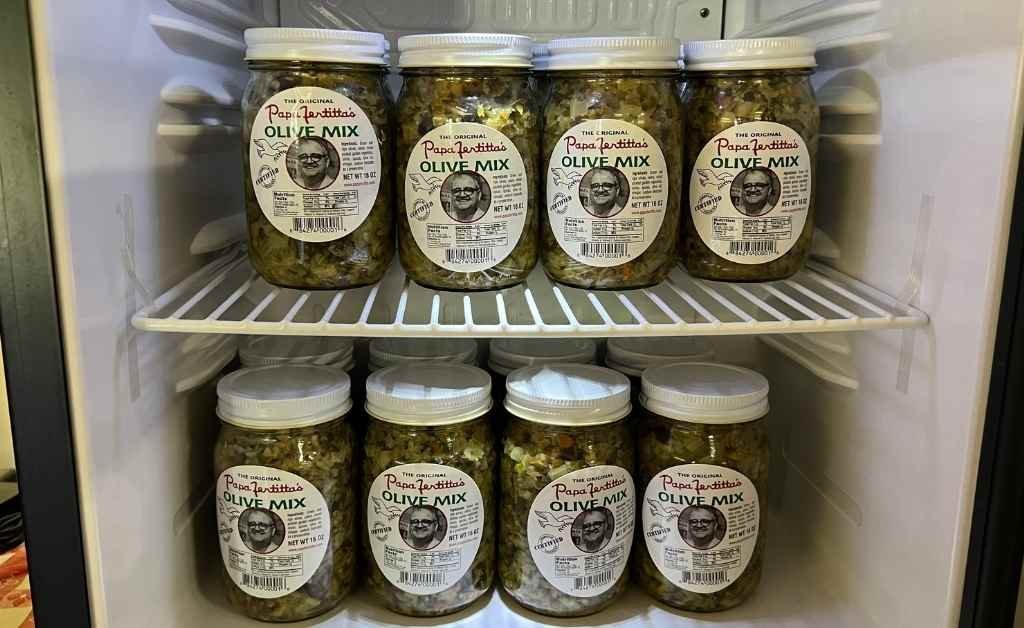 Jars of Papa Fertitta's Original Olive Mix stacked inside a refrigerator, the signature ingredient used in Fertitta's Muffy sandwich.