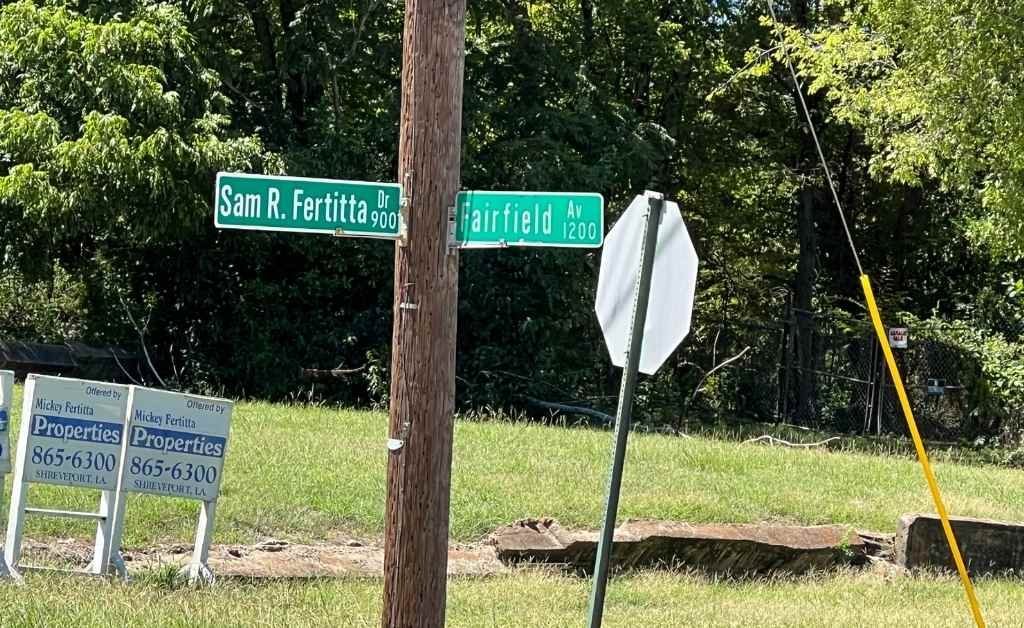 Street signs for Sam R. Fertitta Drive and Fairfield Avenue in Shreveport on a sunny day, marking the legacy of the Fertitta family.