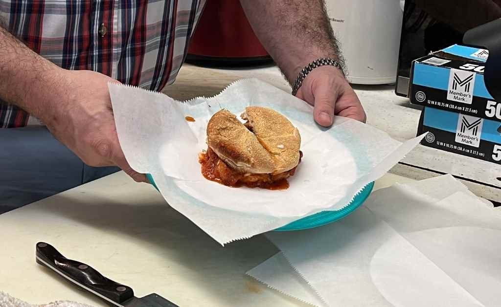 Hands holding the Godfather Sandwich at Fertitta's Deli in Shreveport, featuring Reverend Patrick Fertitta's trademarked alligator Italian sausage known as the Boss of the Bayou.