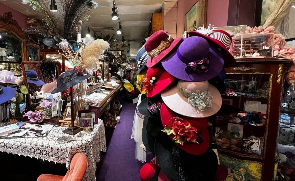 A vibrant display of custom hats at Yvonne LaFleur’s boutique in New Orleans, featuring silk flowers, vintage trims, and European-inspired details arranged among antique furnishings.