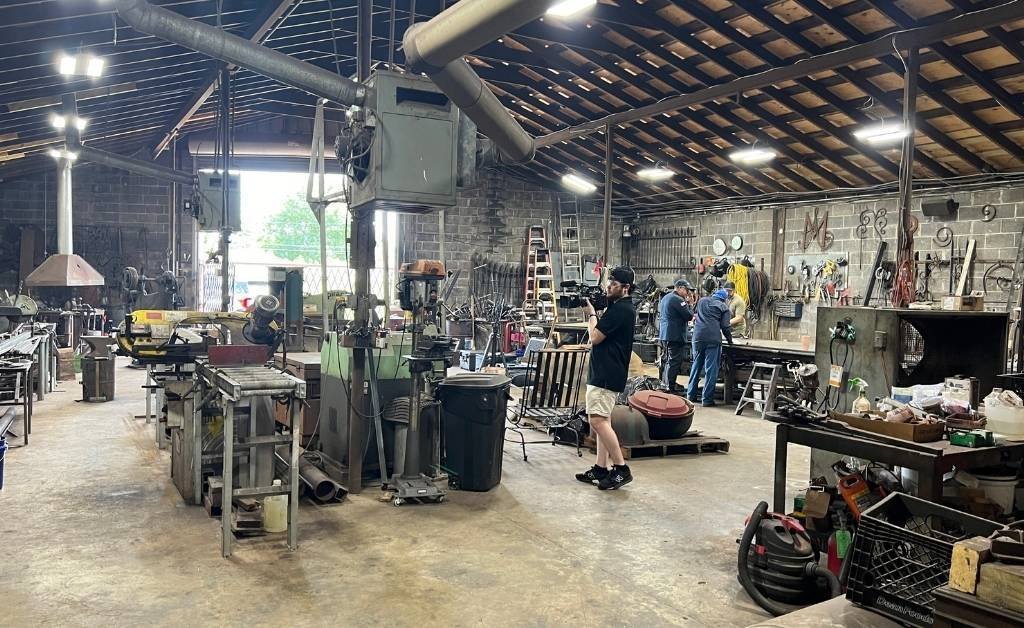 Interior of Darryl Reeves’ 7th Ward blacksmith workshop in New Orleans, filled with tools, machinery, and apprentices learning traditional ironwork.