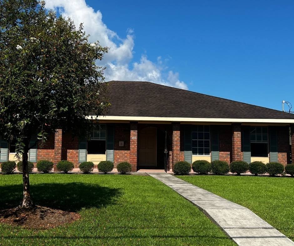 Exterior of the Flooded House Museum in Gentilly, New Orleans, showing the red-brick home with a dark roof, front lawn, and walkway leading to the entrance, preserved as a memorial to Hurricane Katrina’s floodwall breach.