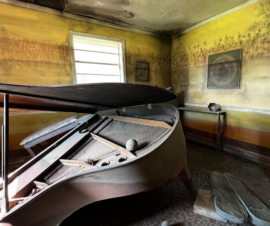 Flood-damaged grand piano inside the Flooded House Museum in New Orleans, with water-stained yellow walls and debris preserved to illustrate the destruction caused by Hurricane Katrina.