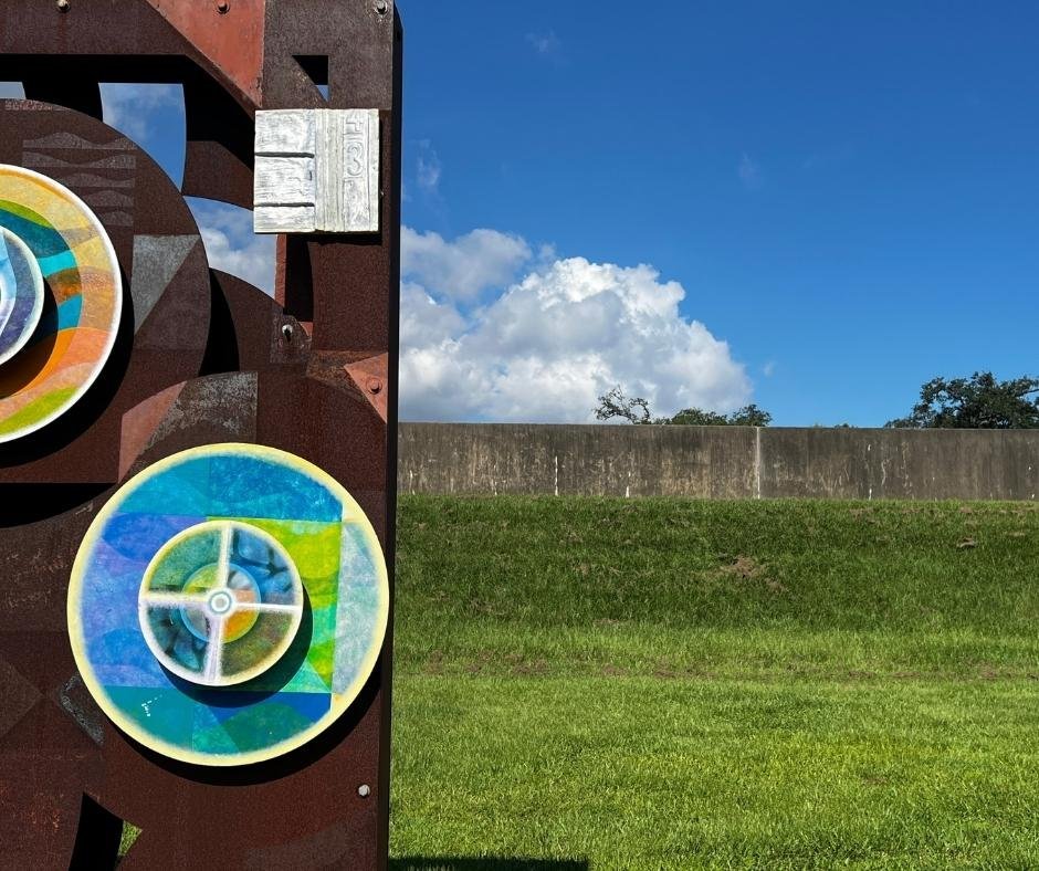 Colorful circular artwork at the Open Air Levee Exhibition in New Orleans, placed near a levee wall under a bright blue sky to symbolize resilience and protection.