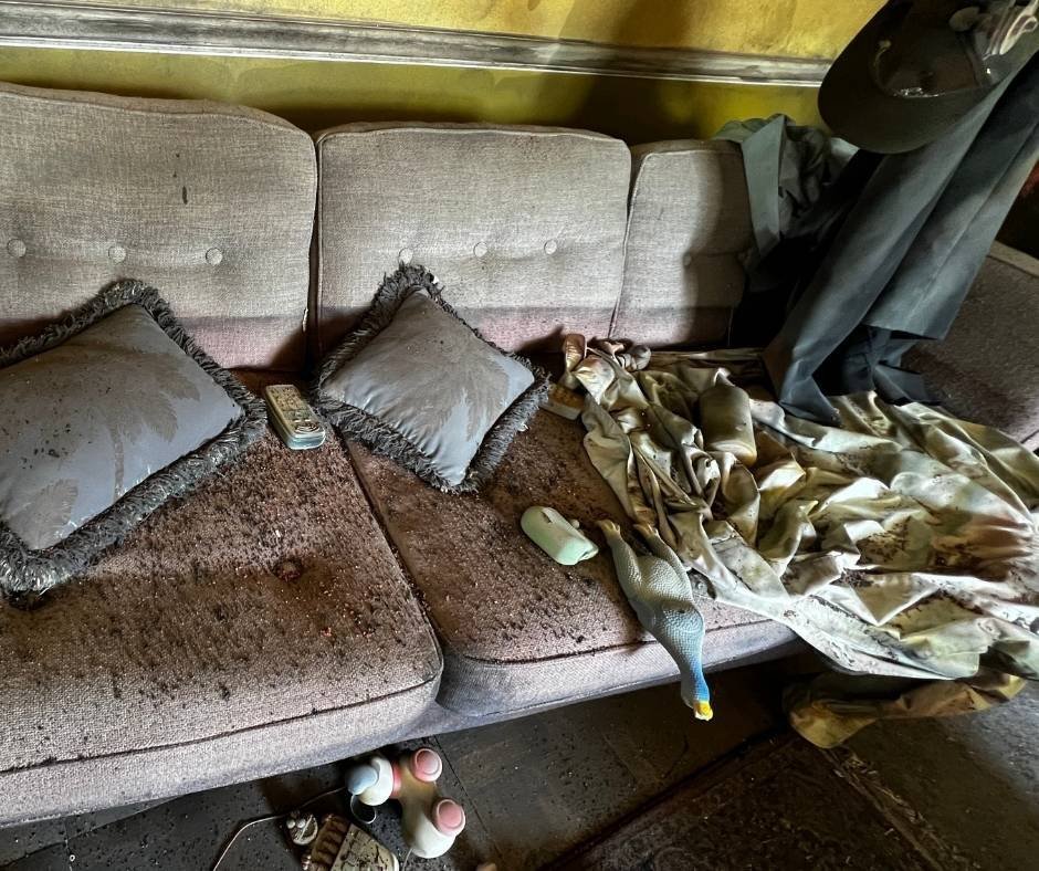 Flood-damaged sofa inside the Flooded House Museum in New Orleans, with water-stained cushions, scattered debris, and a tattered blanket preserved to show the aftermath of Hurricane Katrina.