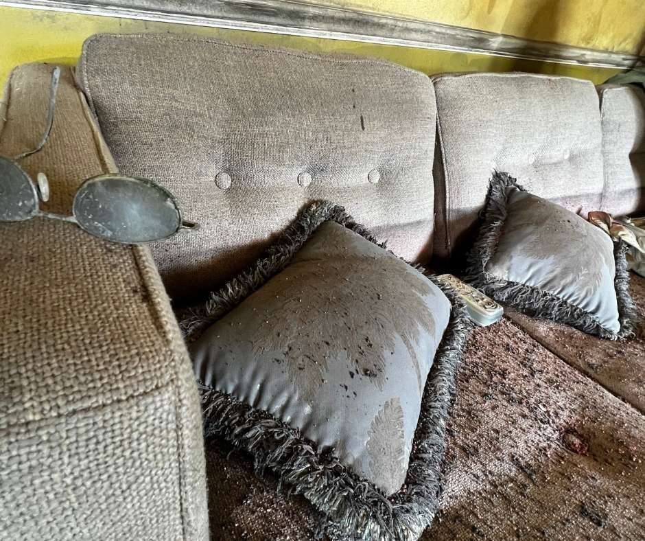 Close-up of a sofa inside the Flooded House Museum in New Orleans, with water-damaged cushions, debris, and a pair of abandoned reading glasses, preserved to illustrate the impact of Hurricane Katrina’s levee failure.