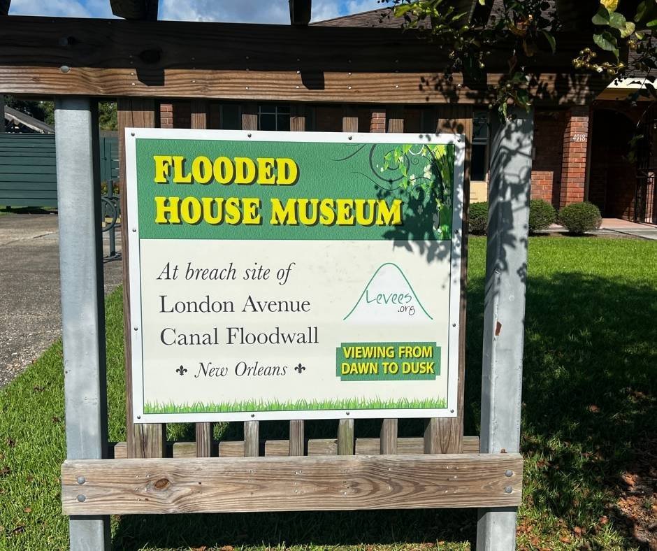 Sign for the Flooded House Museum at the breach site of the London Avenue Canal Floodwall in New Orleans, created by Levees.org, with viewing hours listed as dawn to dusk.