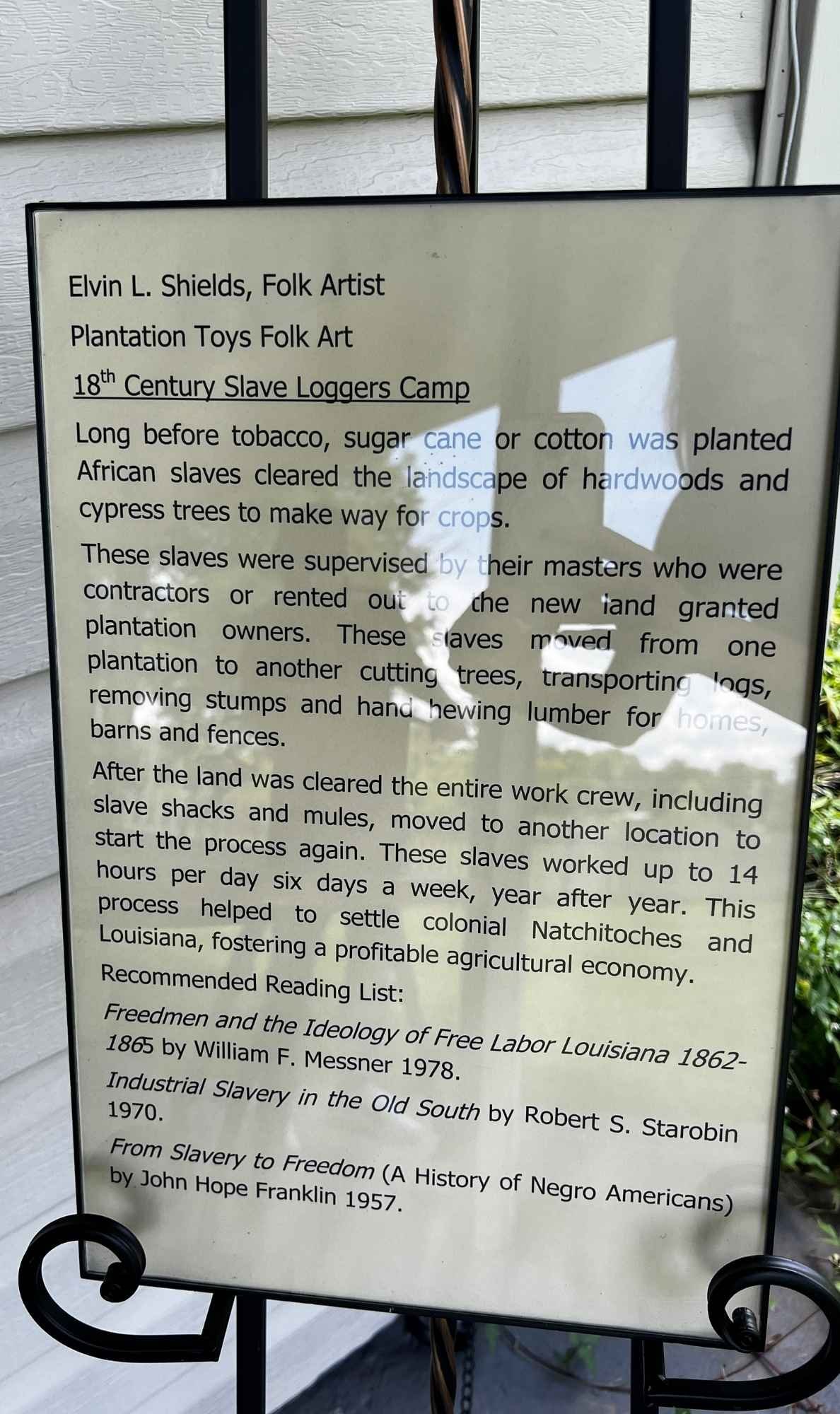 Interpretive panel detailing Elvin Shields’ “Plantation Toys Folk Art” and the legacy of 18th-century slave logger camps in Louisiana.