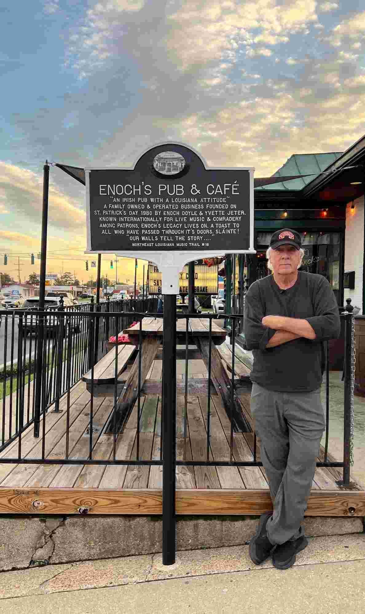 Enoch Doyle Jeter stands beside the official Northeast Louisiana Music Trail marker at Enoch’s Pub & Café, a recognized landmark honoring the region’s musical roots.