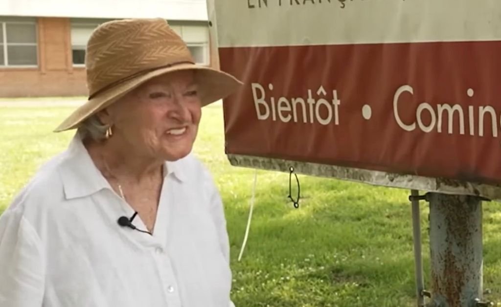 Mavis Arnaud Fruge smiles while standing beside the sign for the future Saint-Luc French immersion school in Arnaudville, Louisiana.