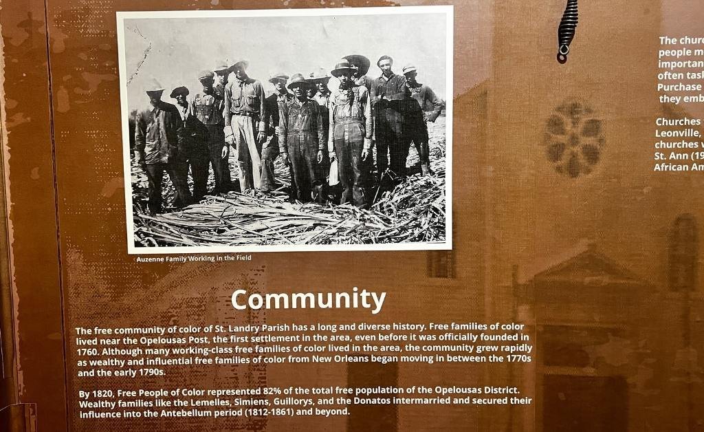 Museum panel titled “Community” with a historical photo of the Auzenne family working in a sugarcane field, highlighting the contributions of free people of color in St. Landry Parish.