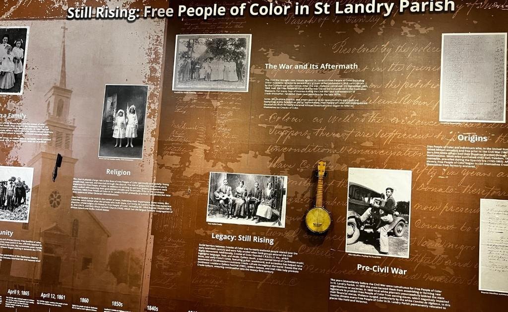 Exhibit panel titled “Still Rising: Free People of Color in St. Landry Parish,” featuring historical photos, documents, and a banjo, highlighting Black heritage and resilience in the region.