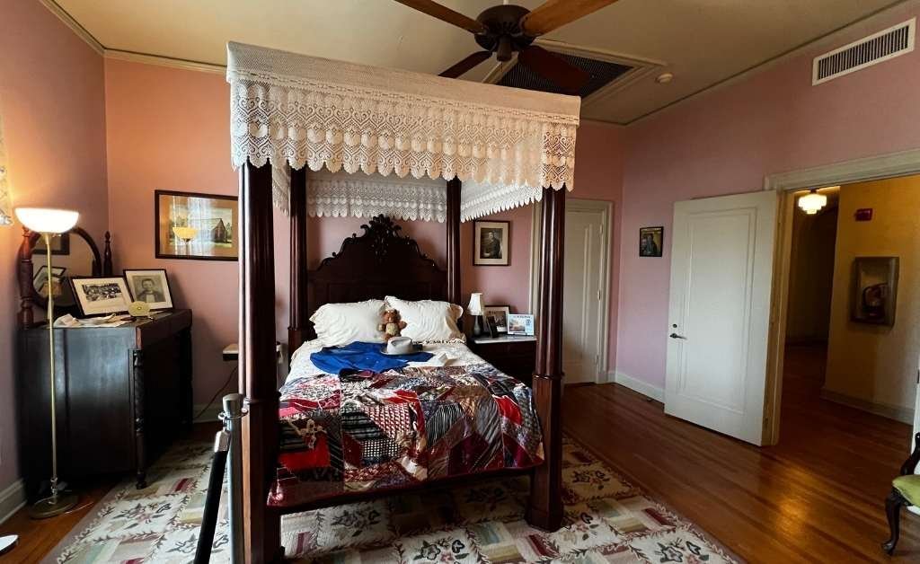 The Jimmie Davis Room inside the Old Governor’s Mansion, featuring a four-poster canopy bed with a colorful quilt made from neckties, vintage furniture, and personal mementos, all preserved to reflect the room’s original lived-in appearance.