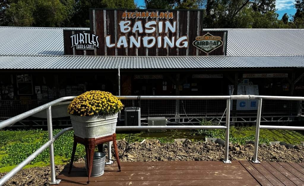Front view of Atchafalaya Basin Landing, featuring the main entrance sign, Turtles Bar & Grill logo, and a metal bucket of yellow flowers on a small platform.