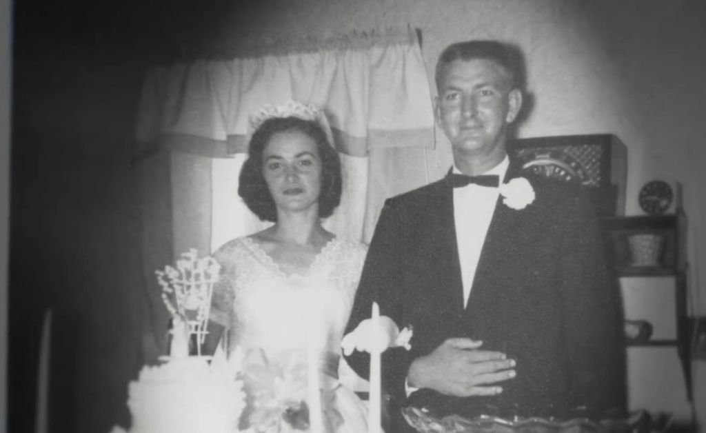 Black-and-white wedding photo of Mavis Arnaud Fruge and her husband, standing beside a tiered cake and candles on their special day.