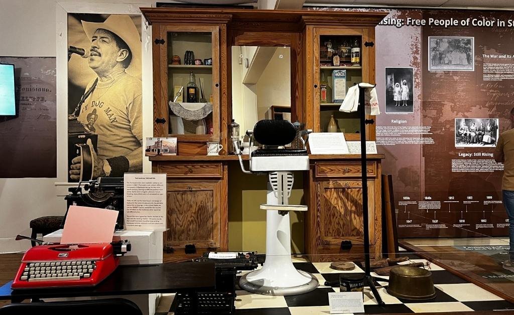 Barbershop-themed museum exhibit with vintage tools, a red typewriter, and interpretive panels highlighting the legacy of Free People of Color in St. Landry Parish.
