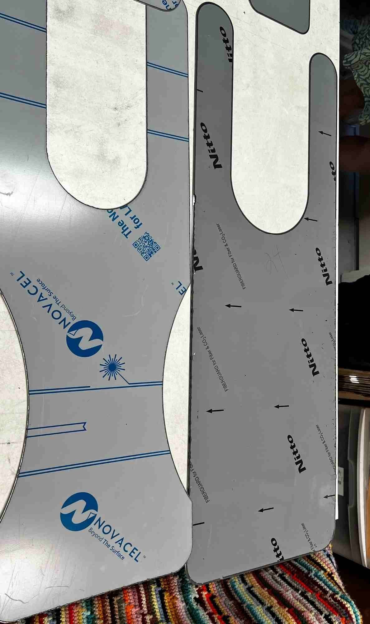Close-up view of unfinished stainless steel rubboard templates on a worktable at Tee Don Landry’s workshop, showing protective film labeled Novacel and Nitto.