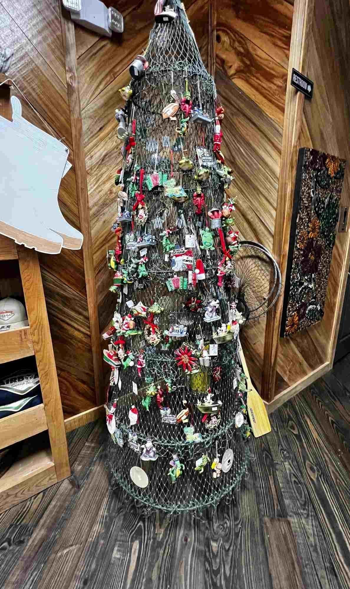 A festive Christmas tree made from a wire crawfish trap, decorated with Cajun-themed ornaments and trinkets, displayed inside the Atchafalaya Basin Landing gift shop.