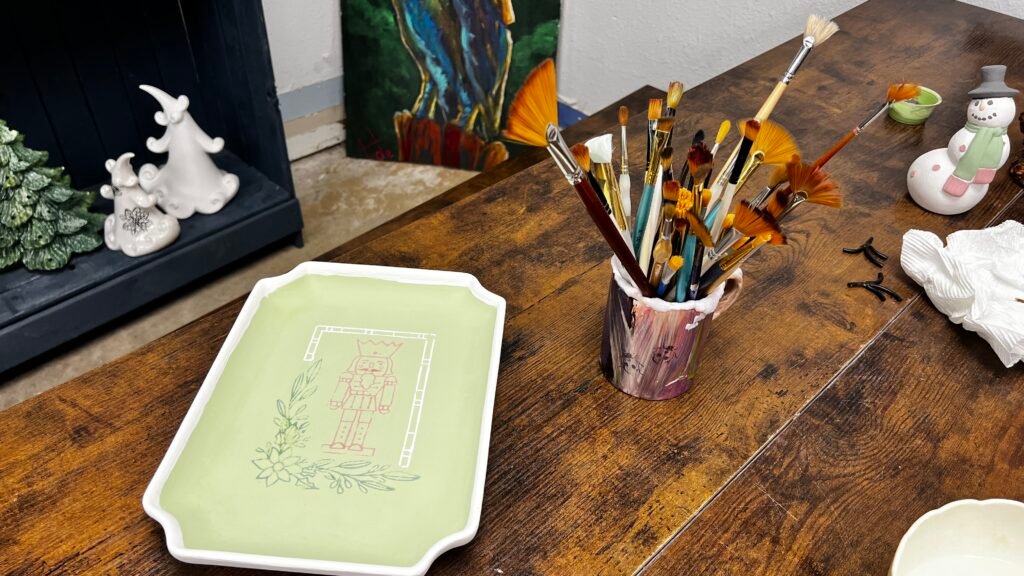 Paint brushes and pottery painting setup on a wooden table at Wrenworks Art Studio in Rivertown Kenner.