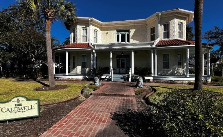 Front exterior of The Caldwell House Bed and Breakfast in Abbeville, Louisiana, showing the historic brick walkway, wrap around porch, and 1907 home facade.