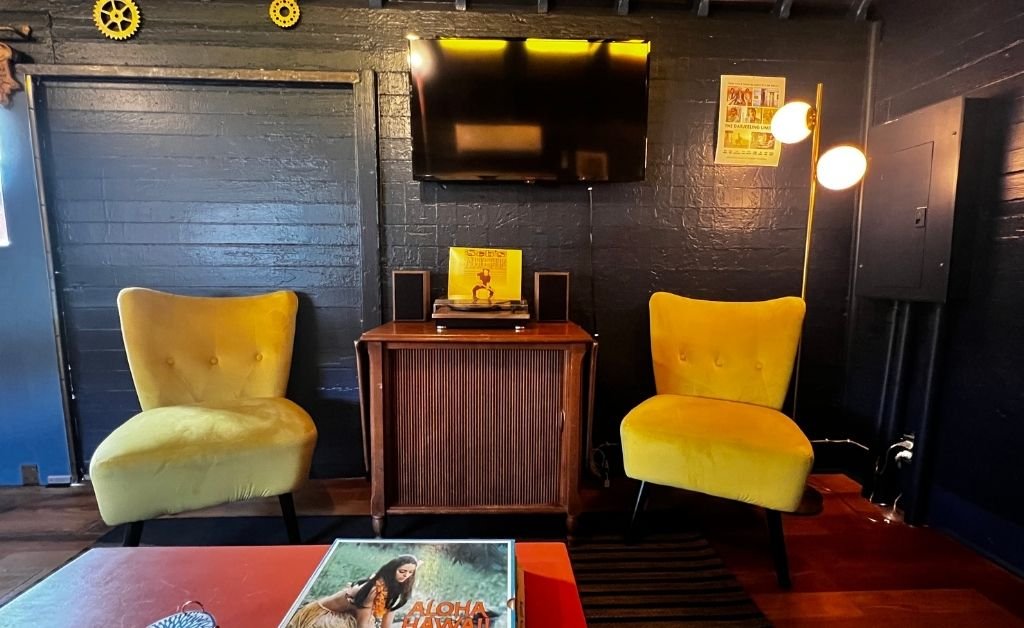 Retro seating area inside the Train Wreck Inn rail car featuring two yellow mid-century chairs, a vintage record console, wall-mounted TV, and warm accent lighting.