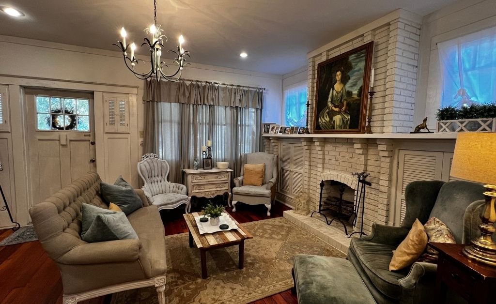 Seating area inside the Clancy House with vintage sofas and chairs, a white brick fireplace, framed artwork, and soft lighting in a restored historic room.
