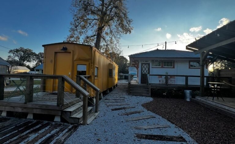 Exterior view of the yellow vintage rail car at the Train Wreck Inn, connected by a gravel pathway and wooden decks to the restored depot building in Grand Coteau, Louisiana. One of the unique place to stay for an authenthc louisiana
