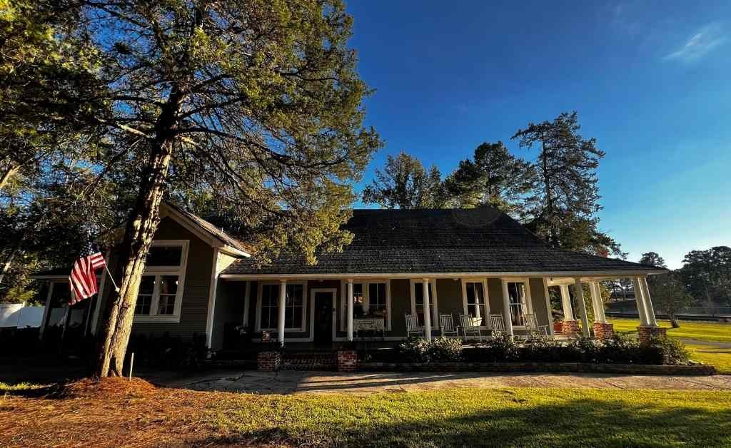 Exterior view of the Dover House in Florien, Louisiana, showing the wraparound porch, columns, and surrounding trees