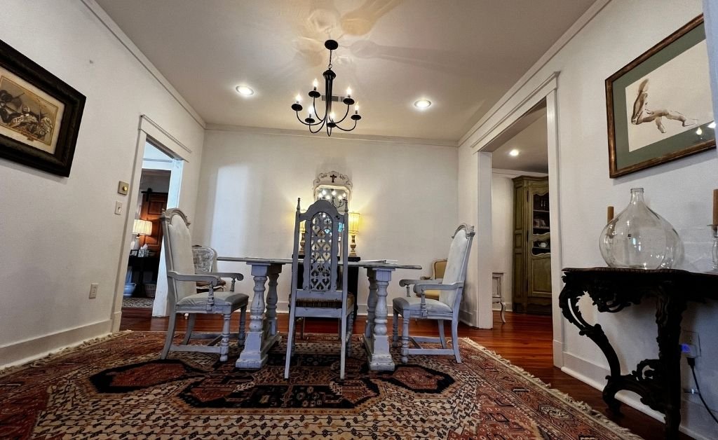 Dining room inside the Clancy House featuring a vintage wooden table and chairs, patterned rug, chandelier, and restored historic details.