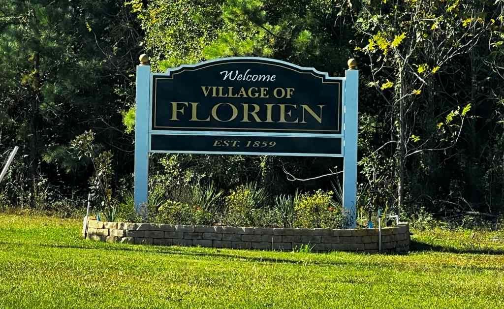 Welcome sign for the Village of Florien, Louisiana, established in 1859, set along a grassy roadside with trees in the background